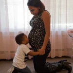 Pregnant mother with son kissing her tummy.