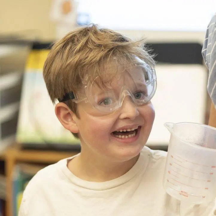 Jubilant young boy with protective eyewear and pitcher of liquid